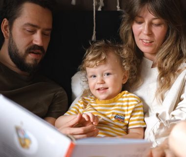 A happy family reading together, featuring parents and their smiling child enjoying a book indoors.